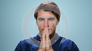 Handsome man praying in studio. Serious guy holding hands in prayer position