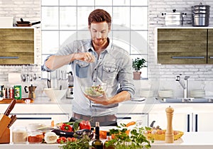 Handsome man preparing salad in kitchen