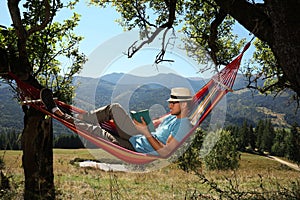 Handsome man reading book in hammock outdoors on sunny day