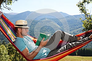 Handsome man reading book in hammock outdoors on sunny day