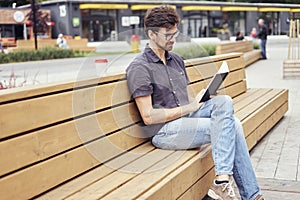 Handsome man reading book sitting outside in public space. Wearing glasses alone working. Concept of education students