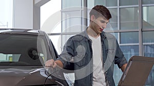 Handsome man reading info paper at car dealership, choosing new auto