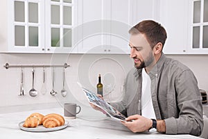 Handsome man reading magazine during breakfast at white marble table in kitchen