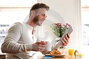 Handsome man reading news on tablet over breakfast