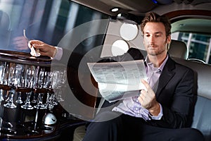 Handsome man reading newspaper in limousine