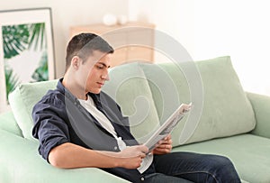 Handsome man reading newspaper on sofa at home