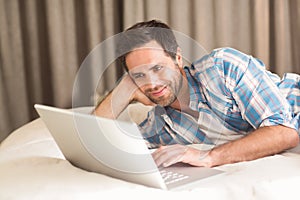 Handsome man relaxing on his bed with laptop