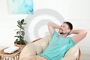 Handsome man relaxing in papasan chair at home, space for text