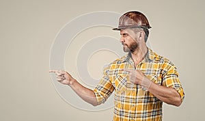 handsome man repairman in construction safety helmet and checkered shirt on building site pointing finegr, copy space