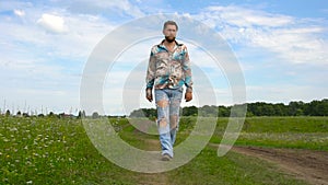 A handsome man in ripped jeans walks around the field alone