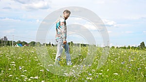 A handsome man in ripped jeans walks around the meadow alone.