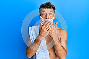 Handsome man saving beard with shave foam over face shocked covering mouth with hands for mistake