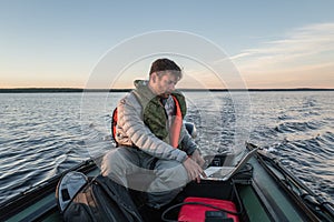 Handsome man is seating in the boat and working with laptop