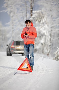 Handsome man setting up a warning triangle and calling for assistance after his car broke down