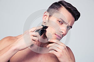 Handsome man shaving with electric razor