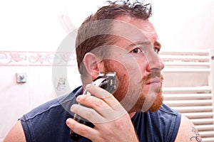 Handsome man shaving face with electric razor