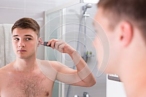 Handsome man shaving his ear with trimmer