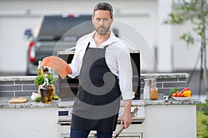 Handsome man in shirt and in cook apron preparing fish on barbecue. Grilling salmon outdoor. Male cook cooking salmon