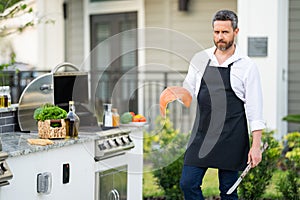 Handsome man in shirt and in cook apron preparing fish on barbecue. Grilling salmon outdoor. Male cook cooking salmon