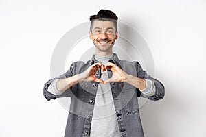 Handsome man showing heart gesture and smiling. Romantic guy say I love you and smiling tender at camera. Valentines day