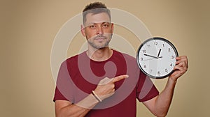 Handsome man showing time on wall office clock, ok, thumb up, approve, pointing finger at camera