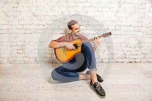 Handsome man siting on floor and playing on the guitar