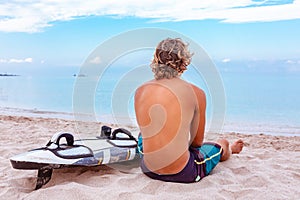 Handsome man sits on the beach with white blank surfing board wait for wave to surf spot at sea ocean shore. Concept of