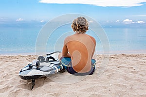 Handsome man sits on the beach with white blank surfing board wait for wave to surf spot at sea ocean shore. Concept of