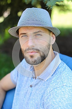 Handsome man sitting in bag chair outside and wearing blue hat.