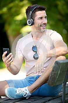 handsome man sitting on bench outdoors and using smartphone