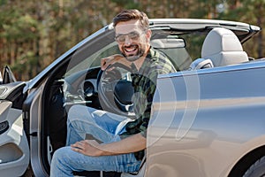 Handsome man sitting in the car with open door and smiling at the camera