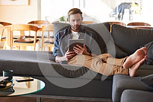 Handsome man sitting with feet on couch holding electronic tablet