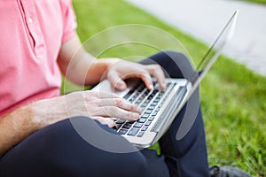 Handsome man sitting on the grass in the city with a laptop, job search