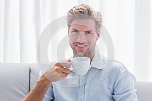 Handsome man sitting on his couch drinking a coffee