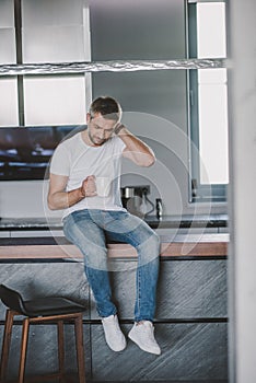 handsome man sitting on kitchen counter and looking in cup