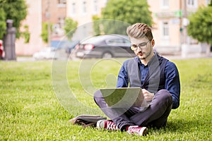 Handsome man is sitting on a lawn and working