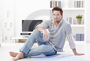 Handsome man sitting on living room floor