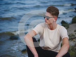 Handsome man sitting near water. A thoughtful guy on a blurred natural background. Male confidence concept. Copy space.