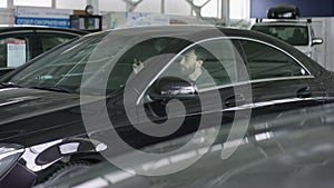 Handsome man sitting in a new car. Successful man examines new auto in auto motorshow. Young bearded customer observe