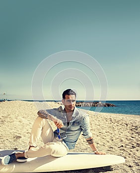 Handsome man sitting on surfboard at beach