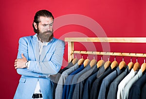 Handsome man in smart casual wear looking at suits and choosing. stylish mens clothing on hanger stand in room. business