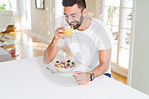 Handsome man smiling eating healthy breakfast and drinking orange juice in the morning