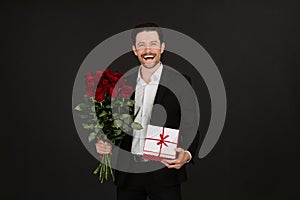 Handsome man smiling and holding present and bouquet with red roses.