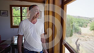 Handsome man smiling looking out the window at winery plantation standing in restaurant indoors. Portrait of proud
