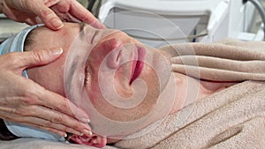 Handsome man smiling to the camera, receiving face massage at spa center