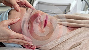 Handsome man smiling to the camera, receiving face massage at spa center