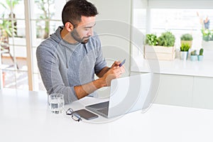 Handsome man smiling using credit card as payment metod when shopping online using laptop