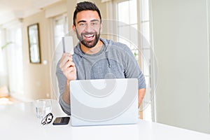 Handsome man smiling using credit card as payment metod when shopping online using laptop
