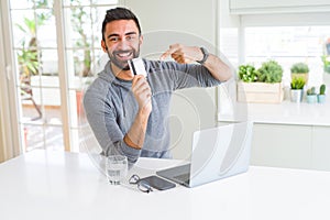 Handsome man smiling using credit card as payment metod when shopping online using laptop