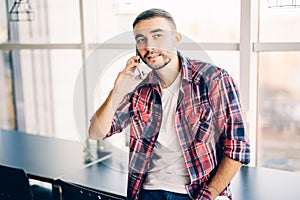 Handsome man speak on phone in office near big windows.